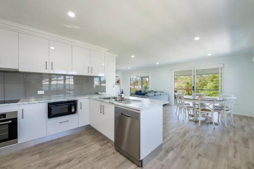 a kitchen with white cabinets and a table with chairs at The Beach House 16 Clarke Street Bargara in Bargara
