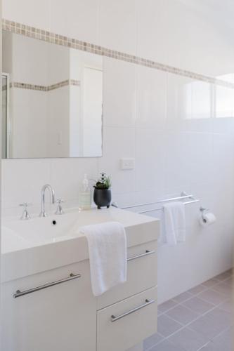 a white bathroom with a sink and a mirror at Ocean Stays - Mollymook in Mollymook