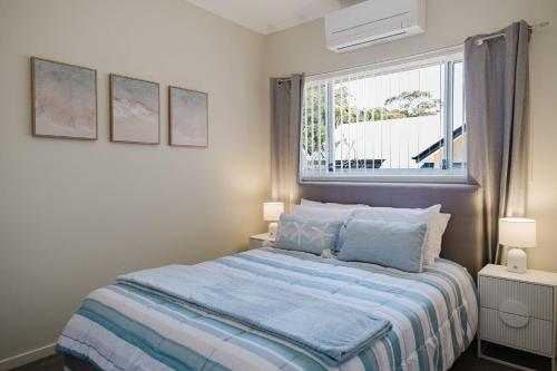 a bedroom with a bed with a blue comforter and a window at Ocean Stays - Mollymook in Mollymook