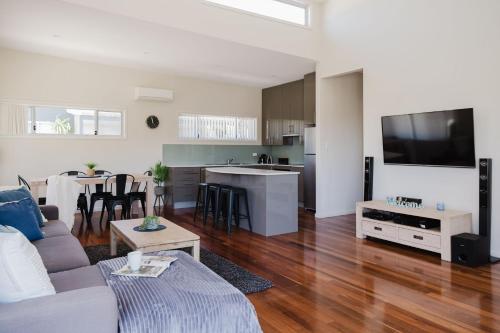 a living room with a couch and a kitchen at Ocean Stays - Mollymook in Mollymook