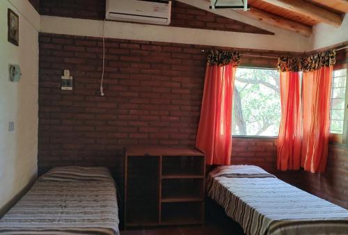 a room with two beds and a window with red curtains at Rincón Soñado in Las Rabonas