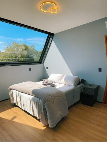 a bedroom with a bed with a large window at Recanto do Tabuleiro chalé com hidro, lareira, churrasqueira e cozinha perto de floripa in Aguas Mornas