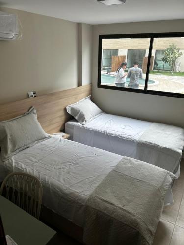 twee bedden in een kamer met twee mensen die uit het raam kijken bij Max Suites block A, apartment 002 in Praia dos Carneiros