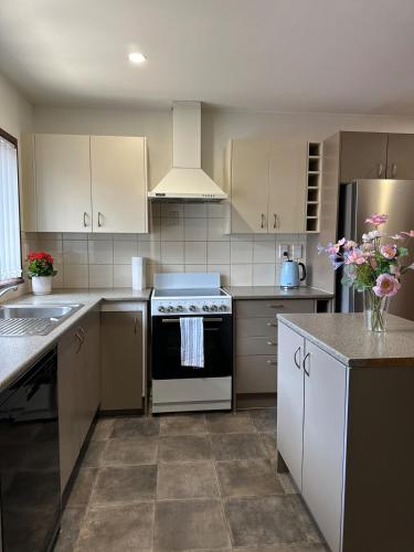 a kitchen with white cabinets and a stove top oven at Carnoustie Calm- A Cosy Wattle Downs Home in Auckland