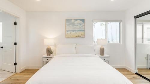 Velvet Sand I by AvantStay Steps to Newport Beach Private Rooftop w Outdoor Kitchen Hot Tub في شاطئ نيوبورت: غرفة نوم بيضاء بسرير كبير ومصباحين