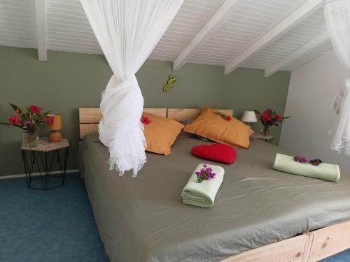 Villa Fleurs d'Air en côte sous le vent في ديساي: غرفة نوم بها سرير كبير وستائر بيضاء ووسائد حمراء