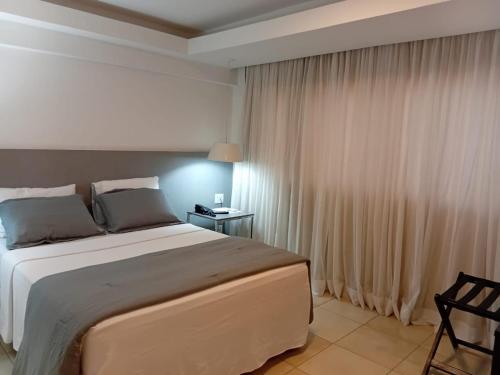a bedroom with a large bed and a window with curtains at Suítes Executivas in Feira de Santana