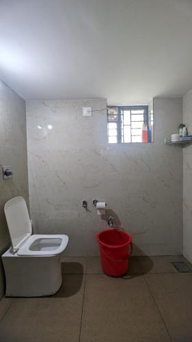 a bathroom with a toilet and a red bucket at REJOICE Homestay - 1BHK private stay in Kalyānpur