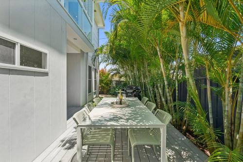 a white table and chairs on a patio with palm trees at The Cheeky Palm - Beachy, enjoy a cheeky cocktail! in Woolgoolga