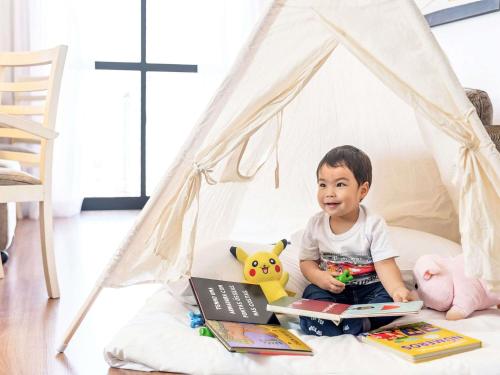 a little boy sitting in a tent reading books at Mercure Sao Paulo Moema in Sao Paulo