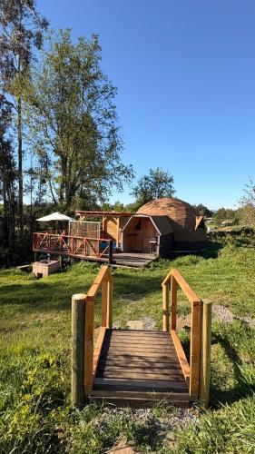 a wooden bridge over a field with a house at Hostal y Domos Bello Horizonte in Villarrica