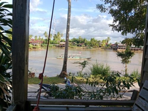 a boat on a river with a palm tree at Boune Hom Guesthouse Sunrise Don Det in Don Det