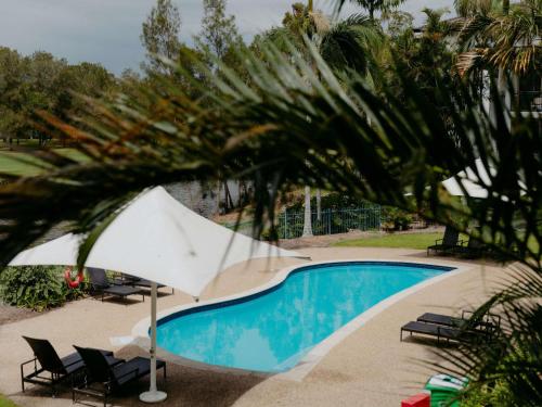 a pool with chairs and an umbrella next to a palm tree at Mercure Gold Coast Resort in Gold Coast