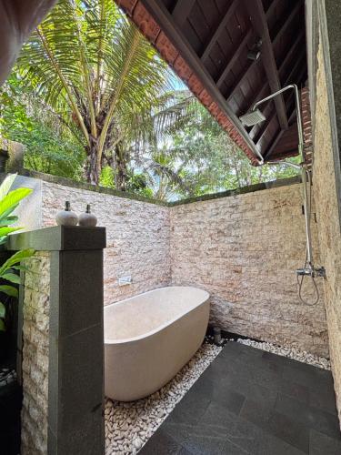 Balian River Hut في Balian: حوض استحمام في حمام مع نخلة