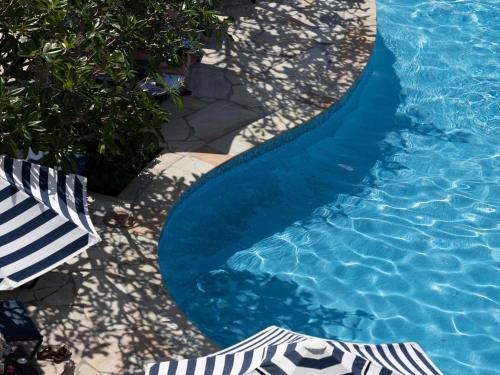 a blue swimming pool with a blue and white umbrella and chairs at Elysium Noosa Resort - MGallery Collection in Noosa Heads