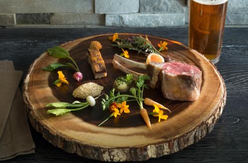 a plate with meat and vegetables on a table with a beer at L'Auberge Provencale Inn & Restaurant in Boyce