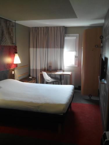 a hotel room with a large bed and a chair at Ibis Aéroport Bâle Mulhouse in Saint-Louis