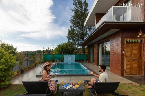 a man and woman sitting on a patio near a swimming pool at EKOSTAY - Terra Cotta Villa in Panchgani