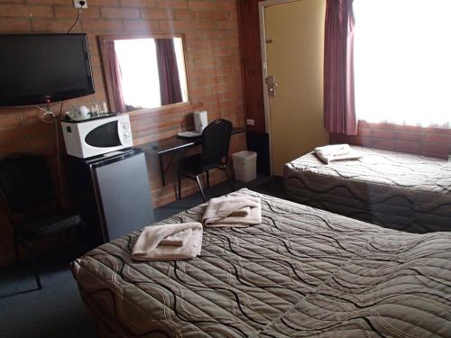 Una habitación de hotel con dos camas, un escritorio y un televisor. en Nhill Oasis Motel, en Nhill