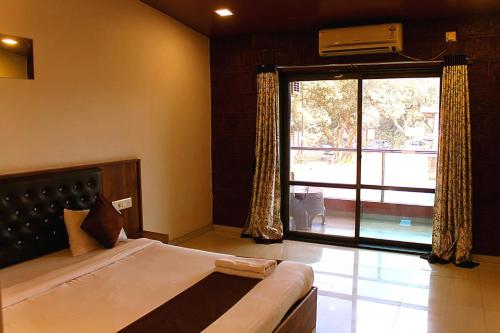 HOTEL GREEN CRYSTAL LINGMALA Mahabaleshwar في ماهاباليشوار: غرفة نوم بها سرير ونافذة كبيرة