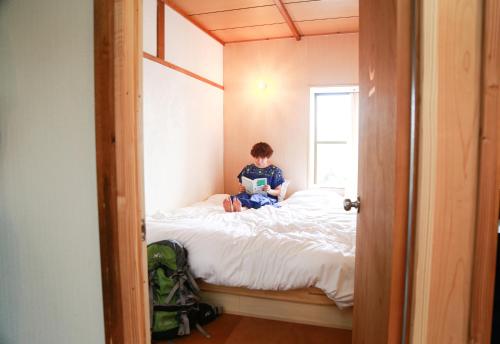a boy sitting on a bed reading a book at Y Pub & Hostel Tottori in Tottori
