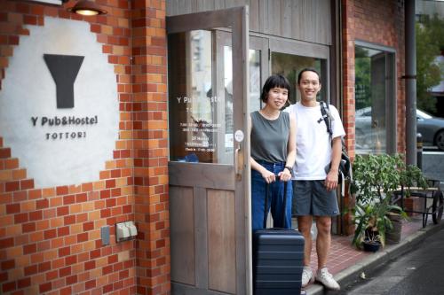 a man and a woman standing outside of a door at Y Pub & Hostel Tottori in Tottori