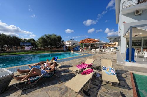 un grupo de personas tumbadas en sillas de jardín junto a una piscina en Hermes Hotel, en Malia