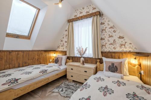 Dos camas en un dormitorio abuhardillado con ventana. en Apartamenty Odkryj-Bialke, en Białka Tatrzanska