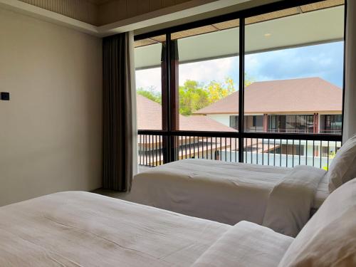 two beds in a bedroom with a large window at Villa Daun Emas in Jimbaran