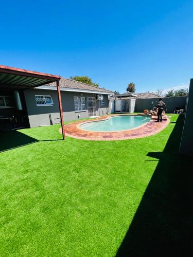 Que Self Catering Apartments - Block7 في غابورون: حديقة خلفية بها مسبح وعشب أخضر
