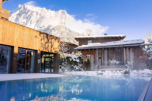 a house with a swimming pool with a snow covered mountain at Bergresort Zugspitze Ehrwald by ALPS RESORTS in Ehrwald