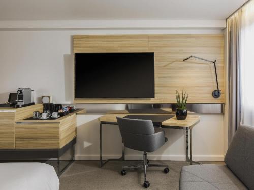 a room with a desk with a television on a wall at Novotel Strasbourg Centre Halles in Strasbourg