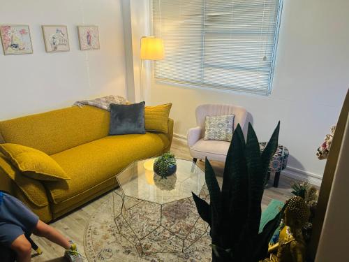a living room with a yellow couch and a glass table at Chic Retreat in Granville - steps to train ! in Clyde