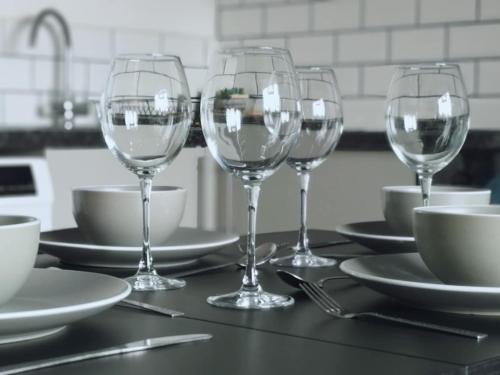 three wine glasses on a table with plates and bowls at Chic 2 Bedroom Apartment-Town Centre-Free Parking in Bournemouth
