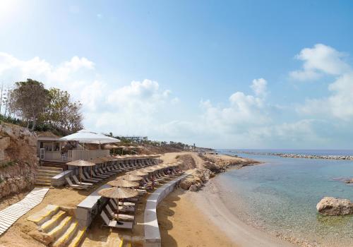 a beach with chairs and umbrellas and the ocean at Leonardo Laura Beach & Splash Resort in Paphos