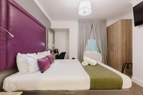 a bedroom with a large bed with a purple headboard at The Porchester Hotel in London