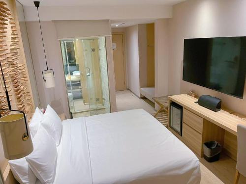 een slaapkamer met een wit bed en een flatscreen-tv bij Orange Hotel Suzhou Emerald Plaza in Suzhou