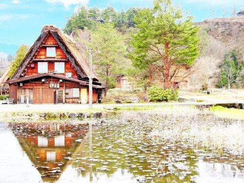 a wooden house sitting next to a large body of water at Oyado Yunosato in Shirakawa