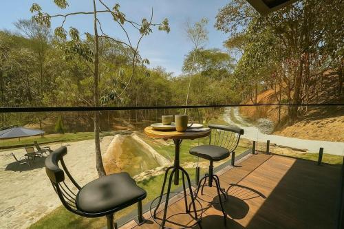 a balcony with a table and chairs and a view of a river at Chalé com banheira, piscina e cachoeira privativa in Taubaté
