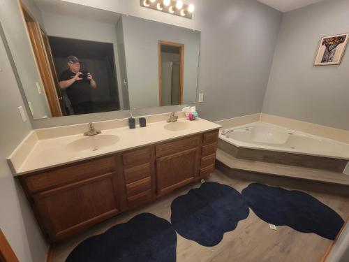 Home away from home في Urbandale: رجل يلتقط صورة للحمام مع مغسلة وحوض استحمام