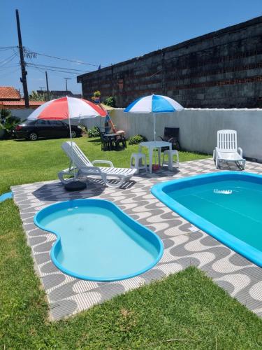 una piscina con due sedie, un tavolo e ombrelloni di Hostel Sepumpá Sepápum a Itanhaém