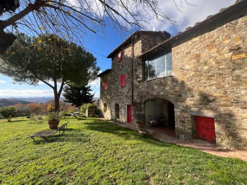 a stone building with red doors on a grass field at Il Fiorino di Badia in Badia A Passignano