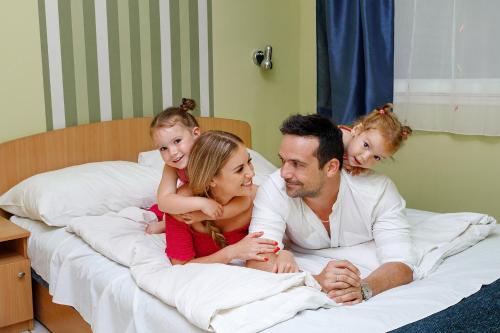 a man and two children sitting on a bed at Ceglédi Apartmanpark & Kemping in Cegléd