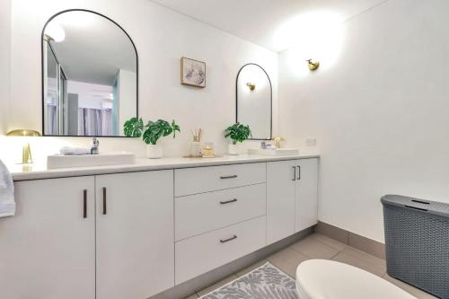 a white bathroom with two sinks and two mirrors at Style, Luxury and Comfort in Larrakeyah in Larrakeyah