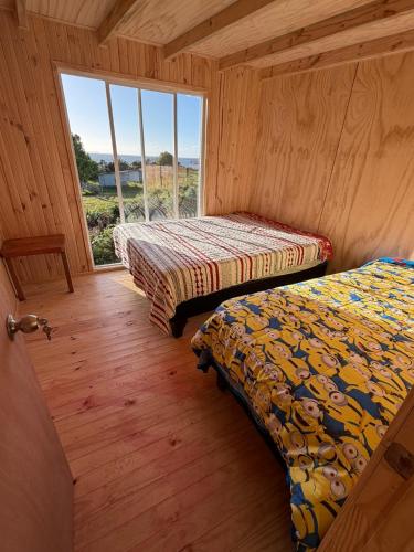 two beds in a room with a large window at Turismo Los Carbooneros de Pugueñun in Ancud