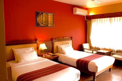 Dragon Nest Resort في Wangdiphodrang: سريرين في غرفة الفندق بجدران حمراء