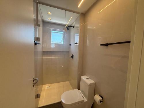 Un baño con inodoro y ducha de cristal. en Apto c/ parrilla a 450 m del mar, Perequê SRF0601, en Perequê