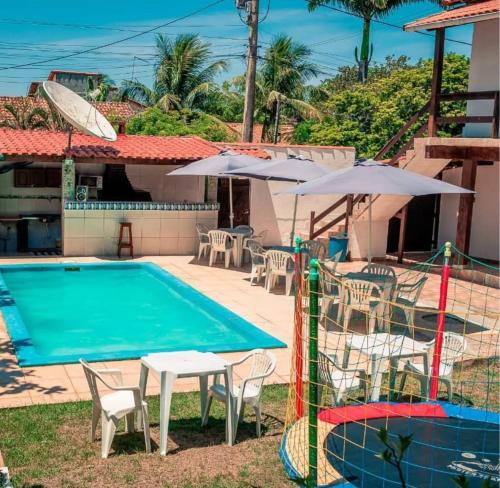Una piscina con mesas y sombrillas al lado de una casa. en Pousada Alto Mar Saquarema, en Saquarema