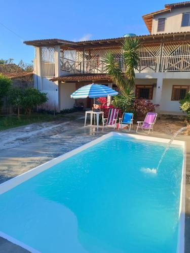 uma piscina com cadeiras e um guarda-sol em frente a uma casa em RESIDÊNCIA MORADA DO SOL em Nova Viçosa