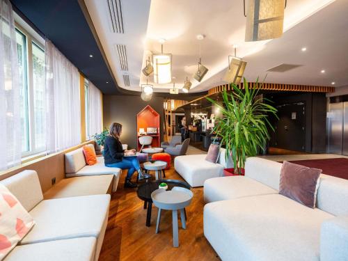 une femme assise dans une pièce avec des canapés et des tables dans l'établissement Novotel Suites Colmar Centre, à Colmar